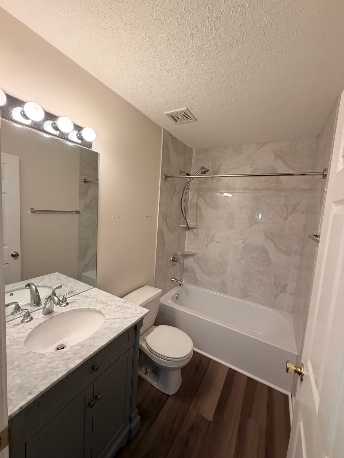 Hall bathroom with a marble-look tub surround, vanity and vinyl plank flooring by SAS Home Solutions