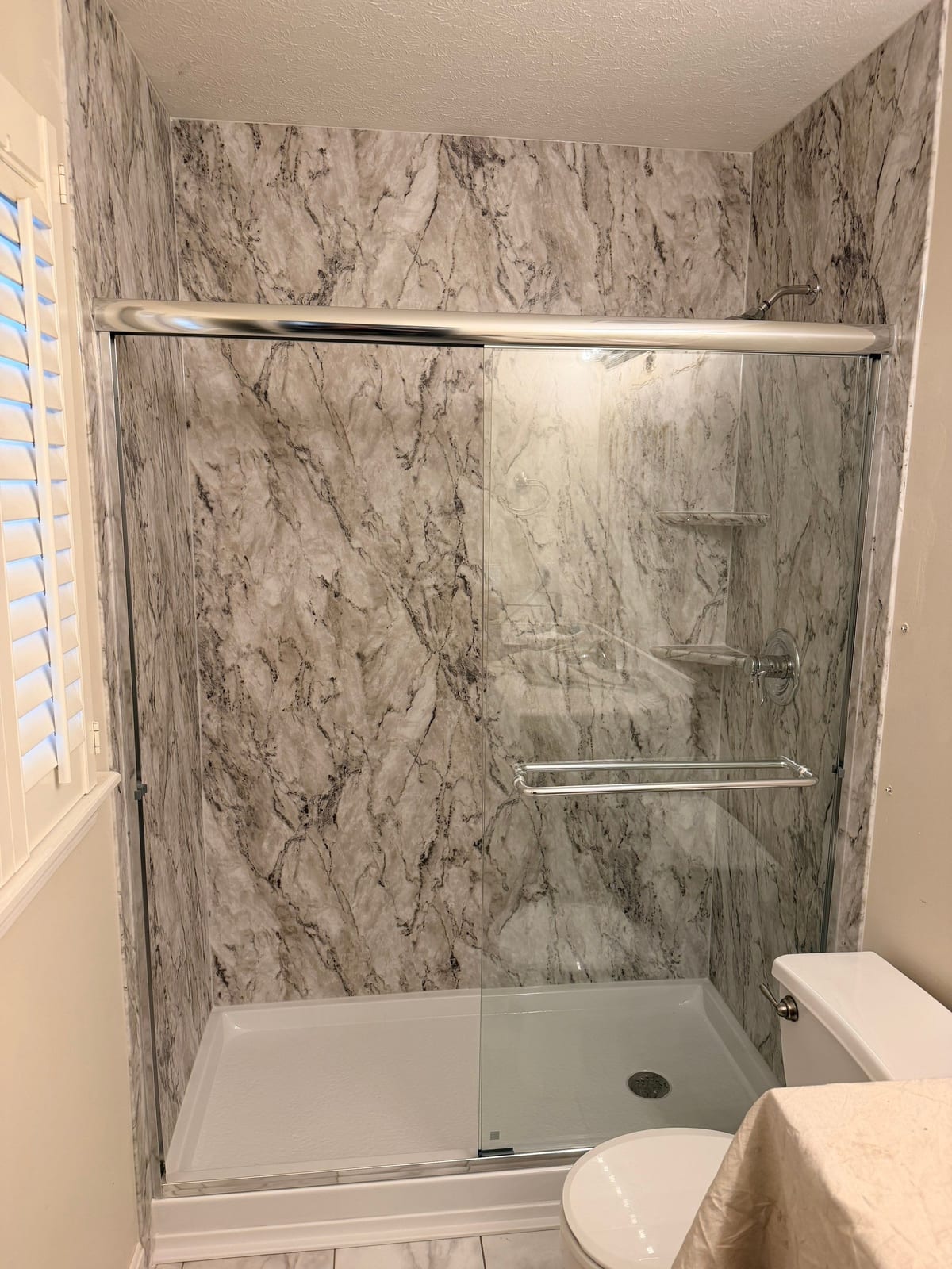 Master bathroom walk-in shower with a marble-look surround and sliding glass door by SAS Home Solutions
