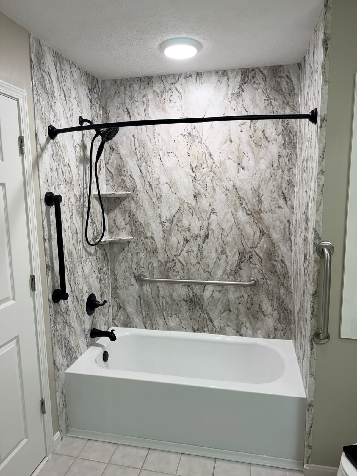 The same tub alcove after a marble-look acrylic surround and matte black fixtures were installed by SAS Home Solutions