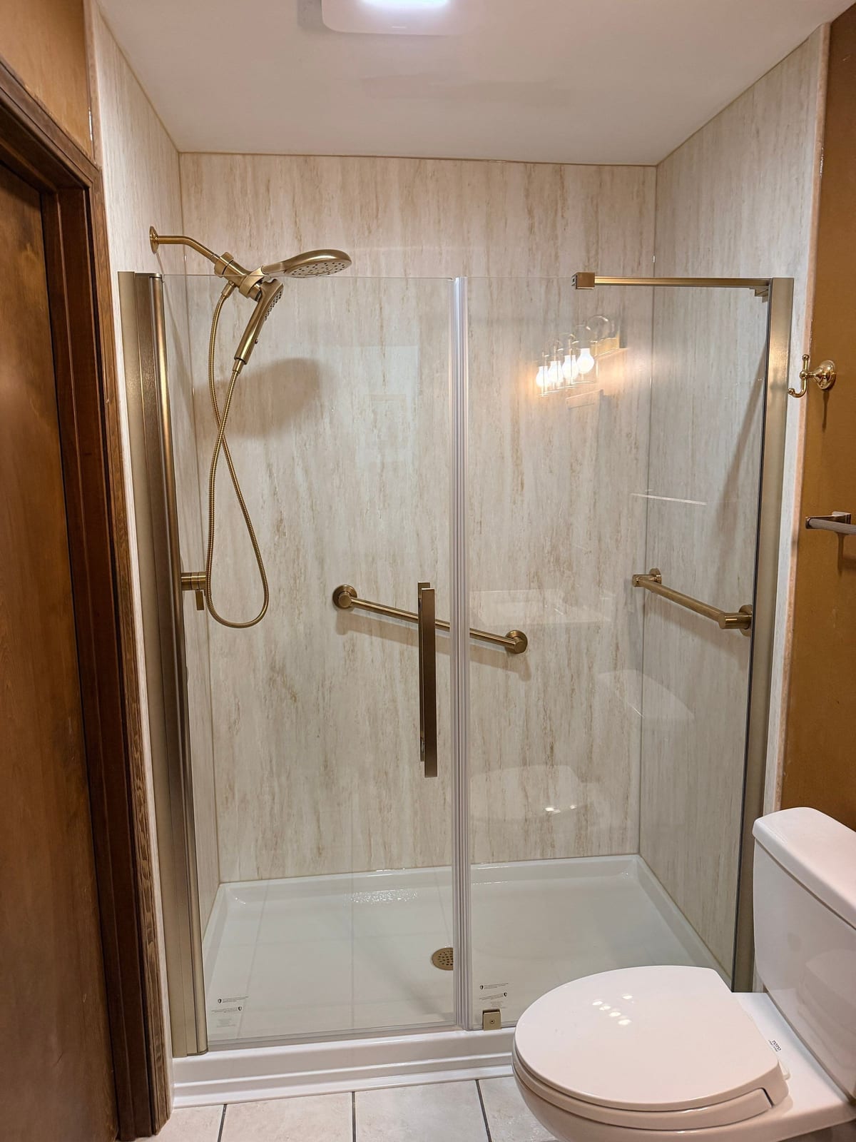 The same shower after a stone-look surround, champagne fixtures and a sliding glass door were installed by SAS Home Solutions