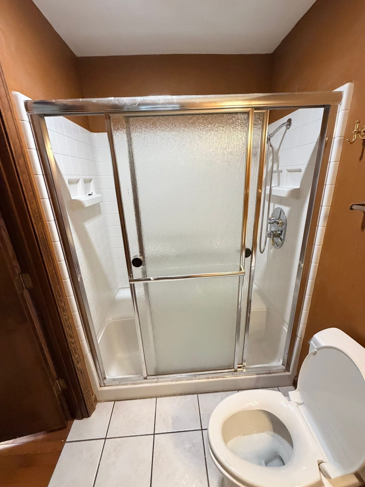 Older shower with framed sliding doors and white tile, before replacement by SAS Home Solutions